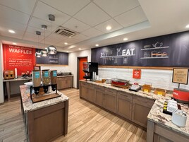 Un área de cocina moderna con una estación de gofres, máquina de café y diversos alimentos exhibidos.
