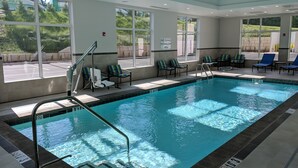 An indoor swimming pool with clear water, surrounded by lounge chairs and large windows offering views of the outside.