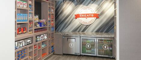 A snack bar with shelves stocked with various snacks and drinks, a refrigerated display case, and a 'Treats' sign on the wall.
