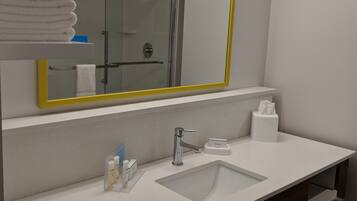A modern bathroom with a large mirror, a sink, and a glass shower enclosure.
