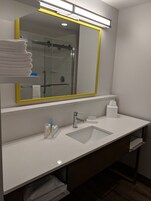Un baño moderno con un espejo grande, un lavamanos y una cabina de ducha de vidrio.