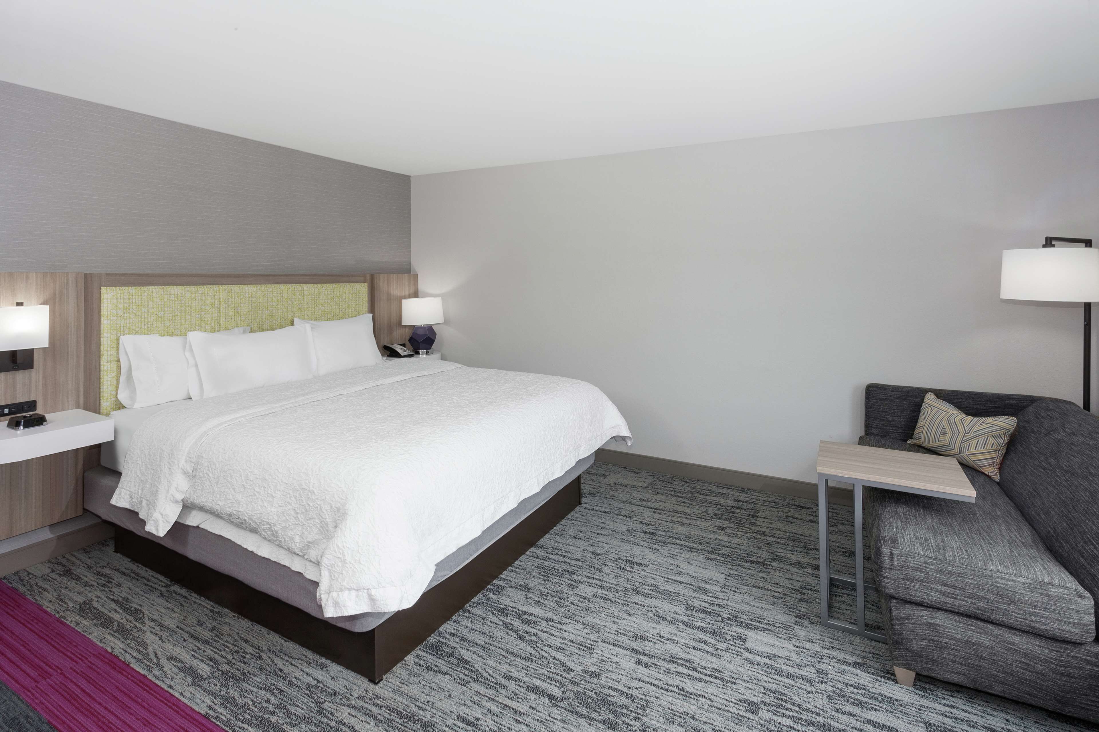 A modern hotel room with a large bed, bedside tables, a sofa, and a small table.