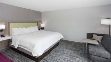 A modern hotel room with a large bed, bedside tables, a sofa, and a small table.