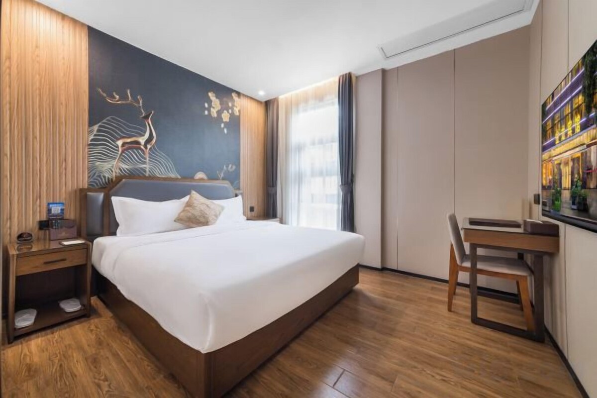 A hotel room with a large bed, a desk, a chair, a nightstand, and a wall with a mural.