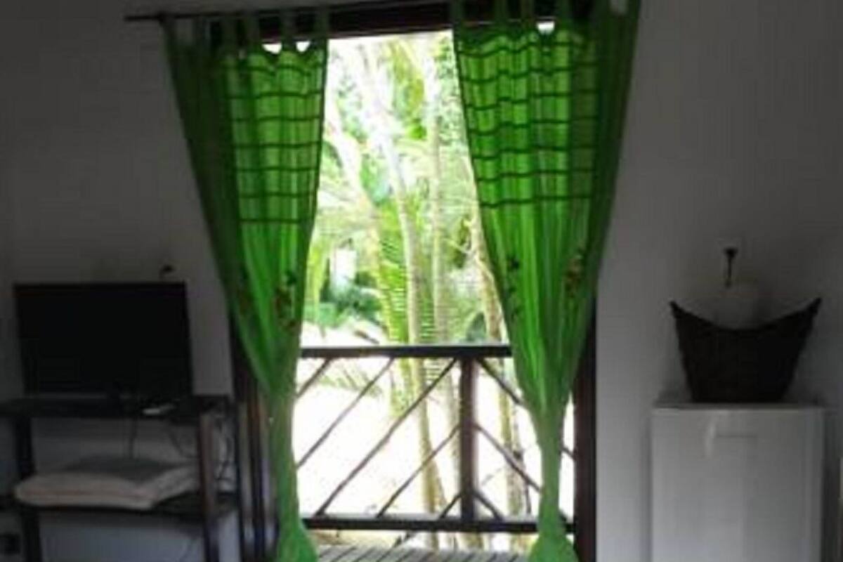 Une pièce avec un lit, une petite table et une fenêtre ornée de rideaux verts.