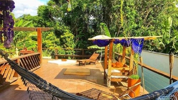A wooden deck with a hammock, a wooden bench, and a small table. - Guest House da Lui (Ubatuba)