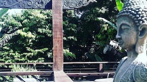 A Buddha statue on a wooden platform with a railing, surrounded by greenery. - Guest House da Lui (Ubatuba)