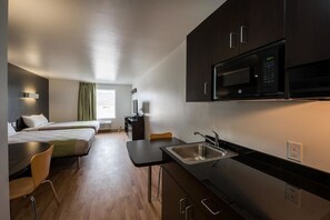 Une chambre d’hôtel de taille réduite, équipée d’une kitchenette, d’un lit, d’un bureau et d’une chaise.