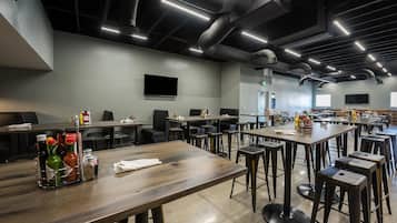 Un restaurante espacioso con techos altos, conductos expuestos e iluminación moderna. Las mesas están dispuestas para grupos, con salsas y servilletas.