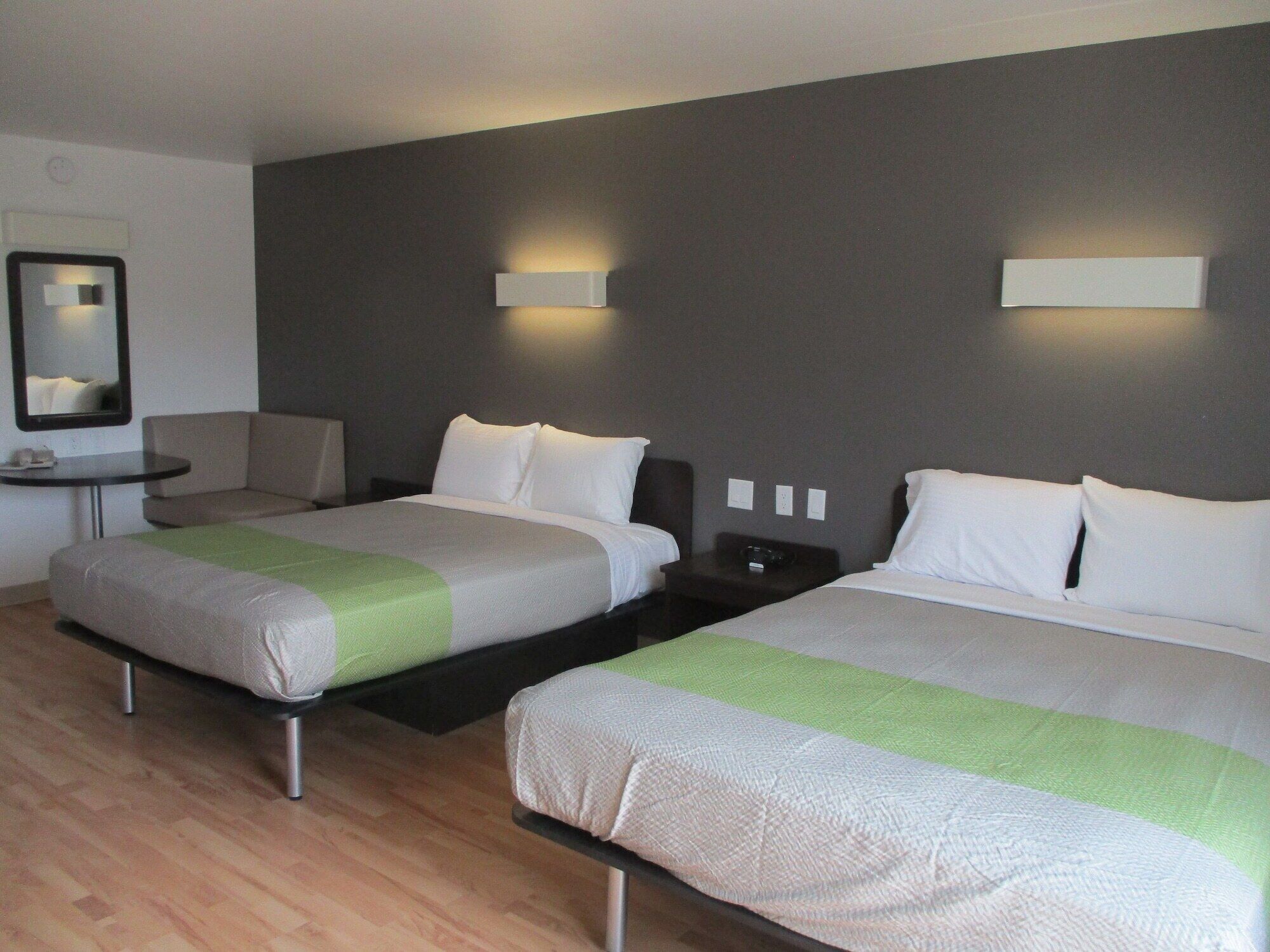 A hotel room with two beds, a small table, a chair, and a mirror.