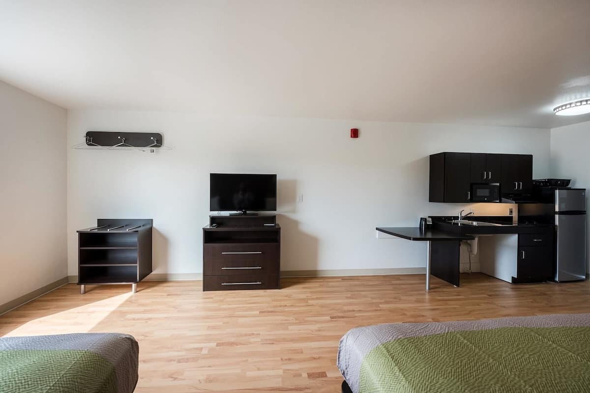 Una habitación pequeña con cama, televisión, kitchenette y un escritorio.