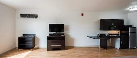 A compact room with a bed, a TV, a kitchenette, and a small desk.