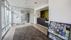 A modern reception area with a glass door entrance, a reception desk, and a wall display of travel brochures. - Studio 6 Mccarran, NV - Sparks - Tahoe - Reno Industrial Center (Sparks)