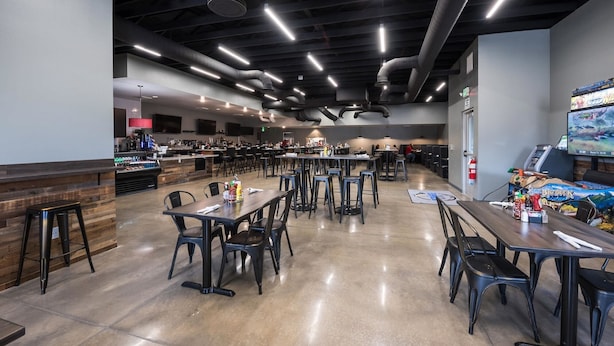 A spacious cafeteria with multiple tables and chairs, a bar area, and a gaming machine. - Studio 6 Mccarran, NV - Sparks - Tahoe - Reno Industrial Center (Sparks)
