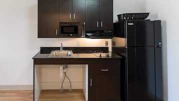 A compact kitchen with dark cabinets, a microwave, a stove, a sink, and a black refrigerator.