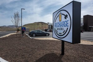 Une enseigne indiquant l’emplacement du « Recharge Bar & Grill », avec une zone de stationnement et un arbre à proximité.