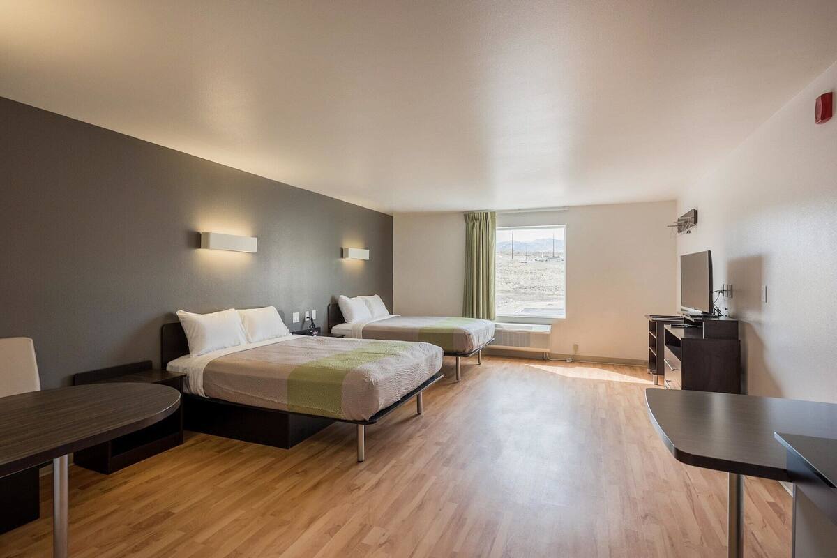 Habitación de hotel con dos camas, televisión, escritorio y ventana con vistas al exterior.