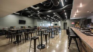 A spacious restaurant with high ceilings, exposed ductwork, and a long bar area.