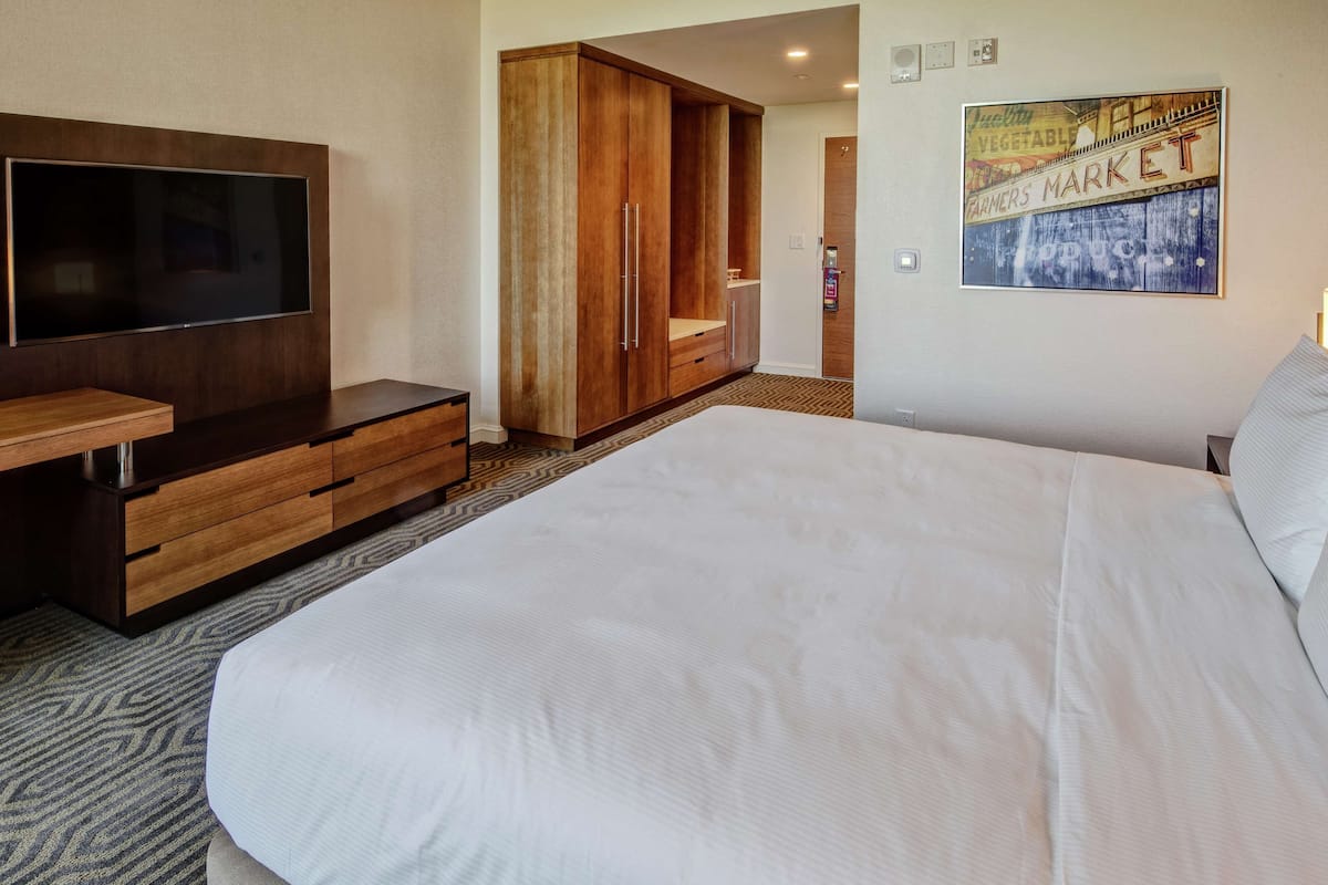 A hotel room with a large bed, a TV mounted on the wall, a wooden wardrobe, and a framed picture on the wall.