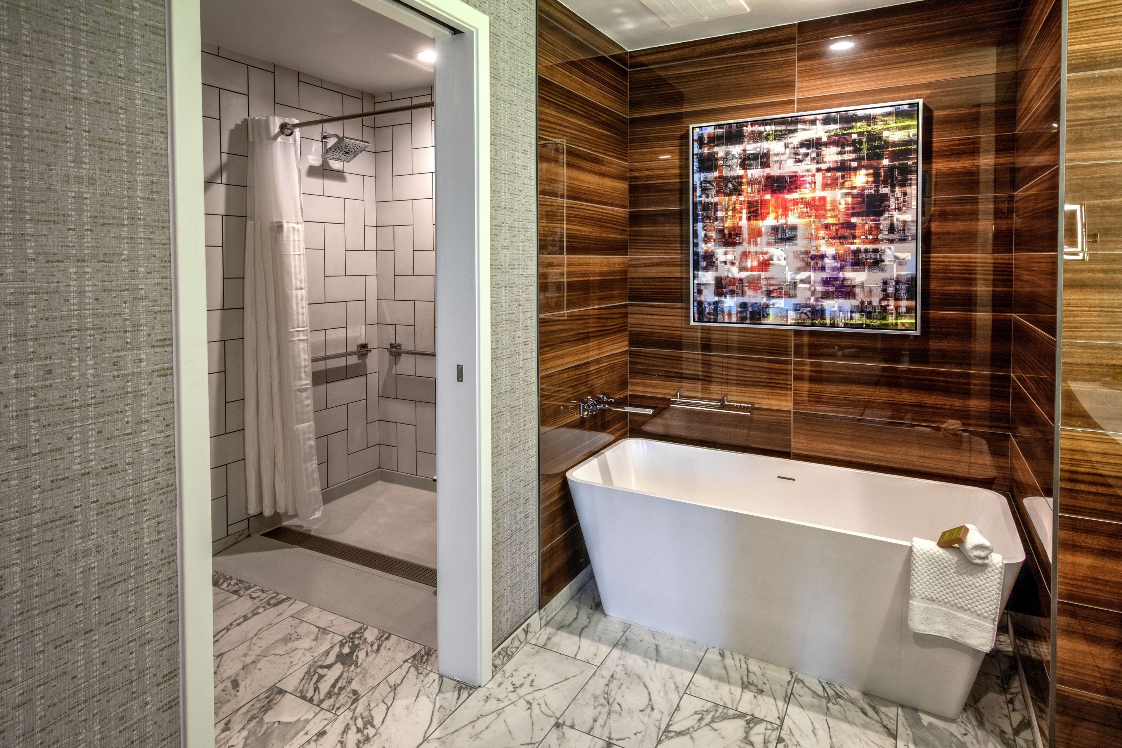 A modern bathroom with a freestanding bathtub, a shower area, and a large mirror with a reflection of the cityscape.