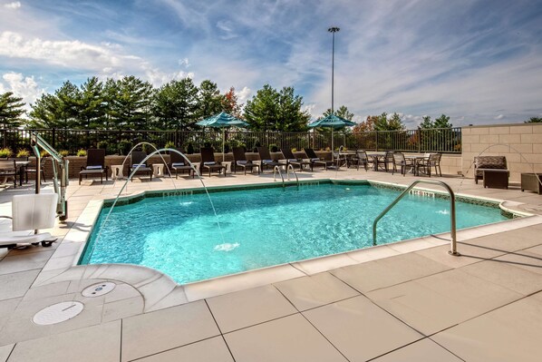 A swimming pool with lounge chairs and umbrellas, surrounded by a fence and trees.