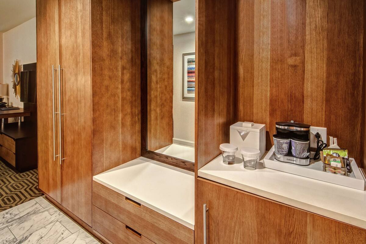 A modern bathroom with wooden cabinetry, a white sink, and a coffee maker on the counter.
