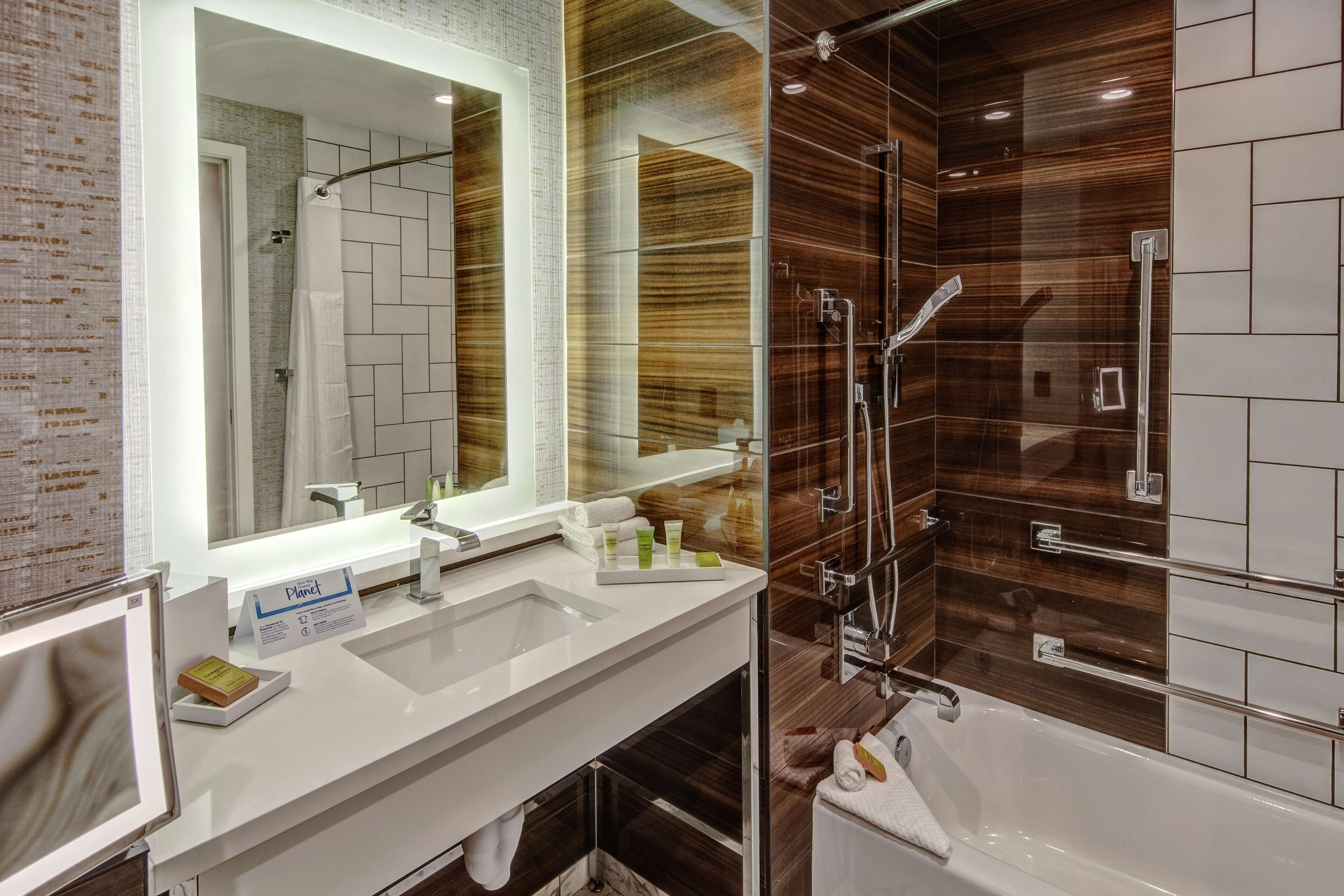 A modern bathroom with a large mirror, two sinks, a shower, and a bathtub.