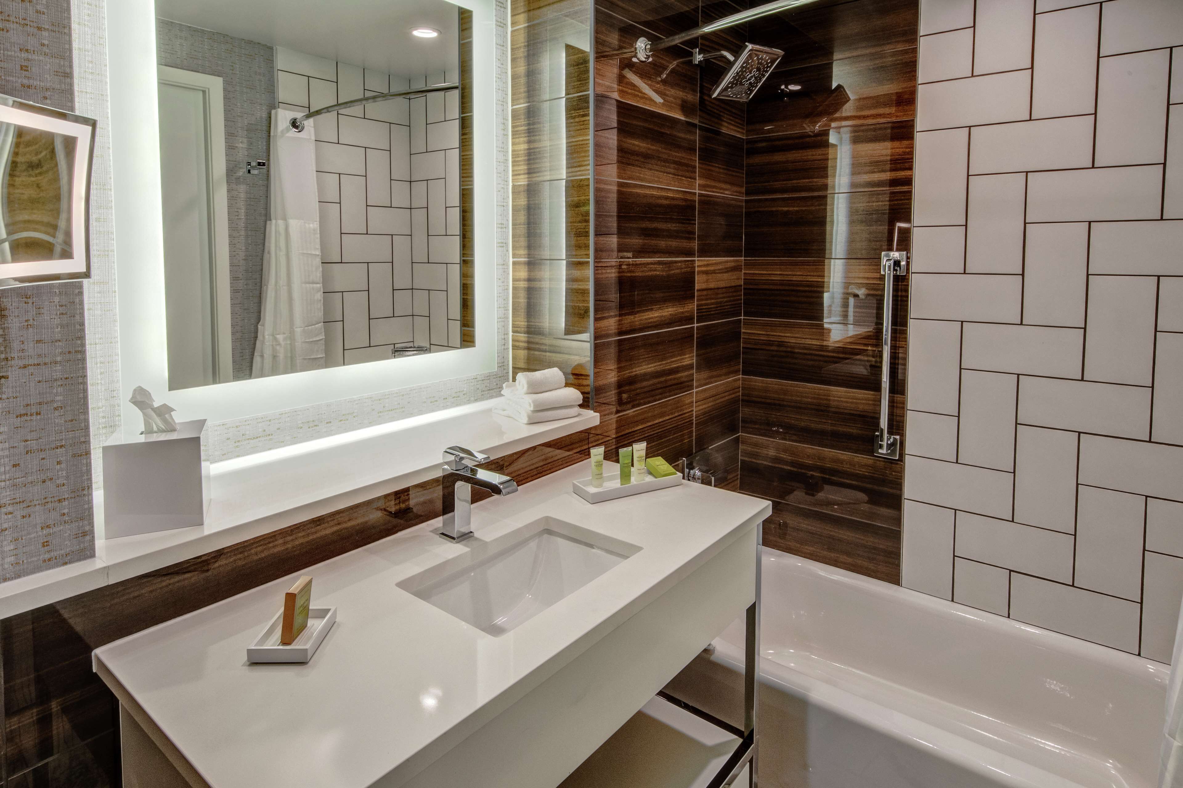 A modern bathroom with a large mirror, two sinks, a bathtub, and a shower area.