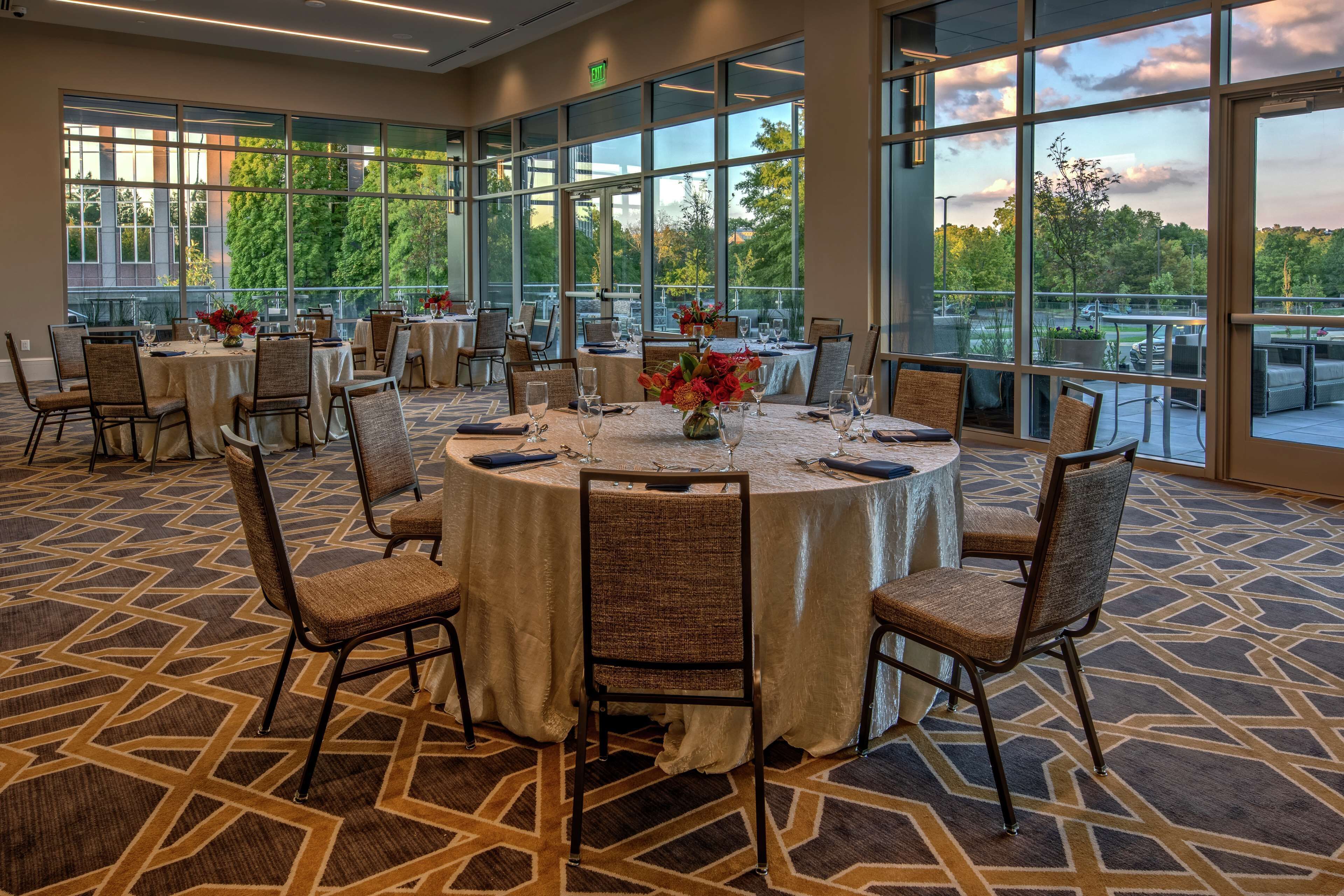 A conference room with round tables, chairs, and large windows offering a view of the outdoors.
