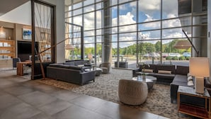 A spacious lobby with a large seating area, a fireplace, and a view of the parking lot. - Hilton Franklin Cool Springs (Franklin)