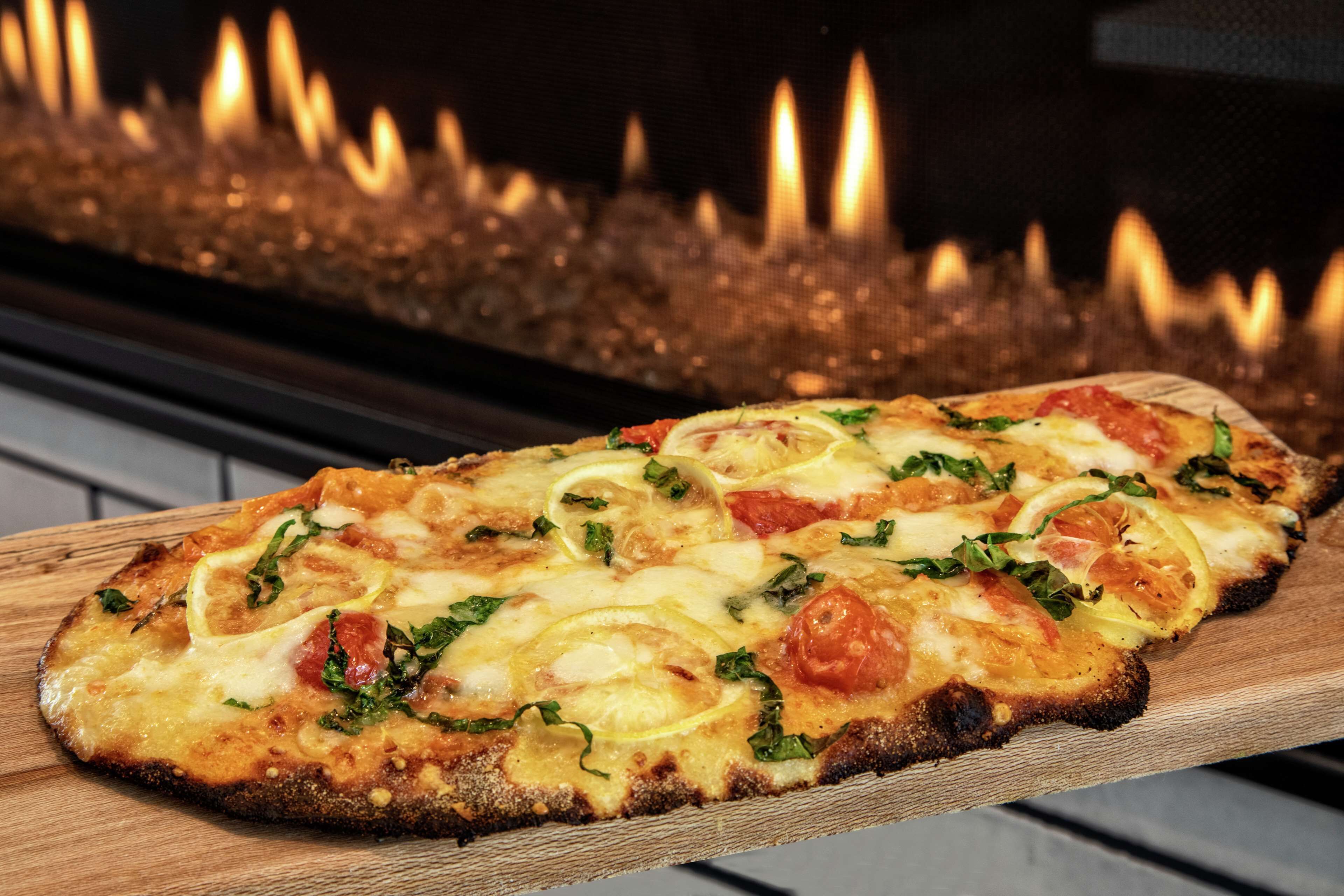 A pizza on a wooden board with a fireplace in the background.