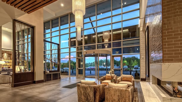 A spacious lobby with a marble reception desk, comfortable seating, large windows, and a modern chandelier. - Hilton Franklin Cool Springs (Franklin)