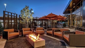 An outdoor seating area with wicker furniture, a fire pit, and umbrellas. - Hilton Franklin Cool Springs (Franklin)