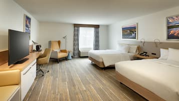 Habitación de hotel con una cama grande, una cama individual, un escritorio con televisor, una silla y una ventana con cortinas.