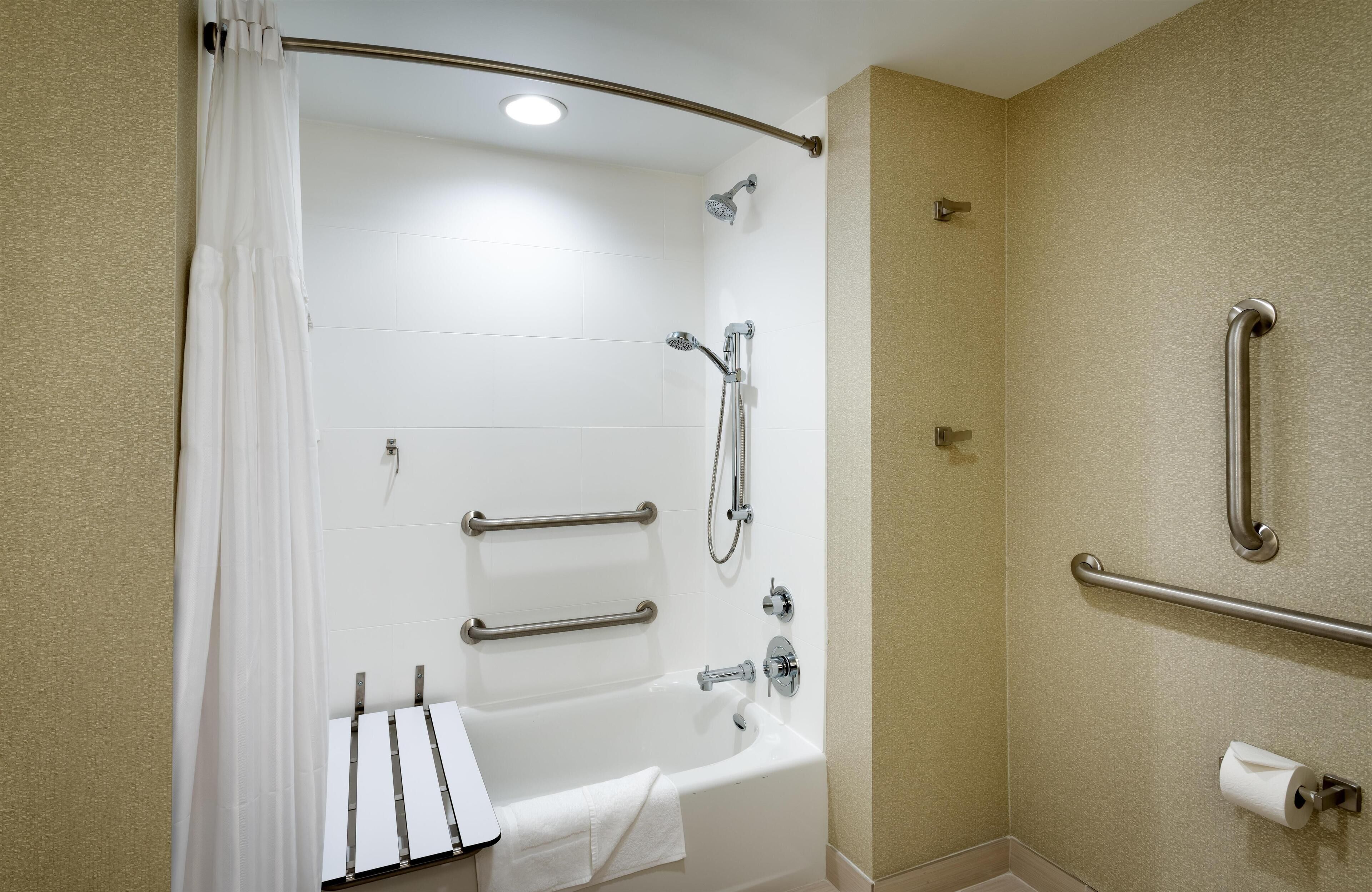 Une salle de bain équipée d’une baignoire, d’une douche, de barres d’appui et d’un porte-rouleau de papier toilette.