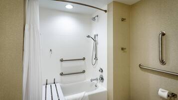 Une salle de bain équipée d’une baignoire, d’une douche, de barres d’appui et d’un porte-rouleau de papier toilette.