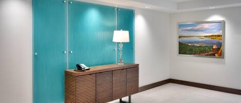 Eine moderne Lobby mit einem türkisblauen Raumteiler, einem Holzkonsolentisch mit Lampe und einem gerahmten Landschaftsbild an der Wand.