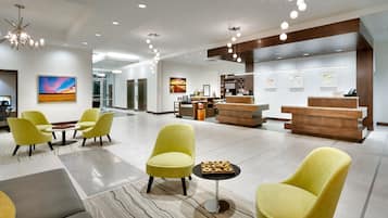 A hotel lobby with yellow chairs, a reception desk, and artwork on the walls.