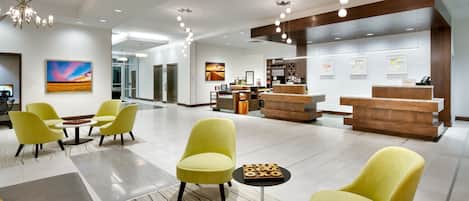 Et hotellobby med gule stole, en receptionsdisk og kunst på væggene.