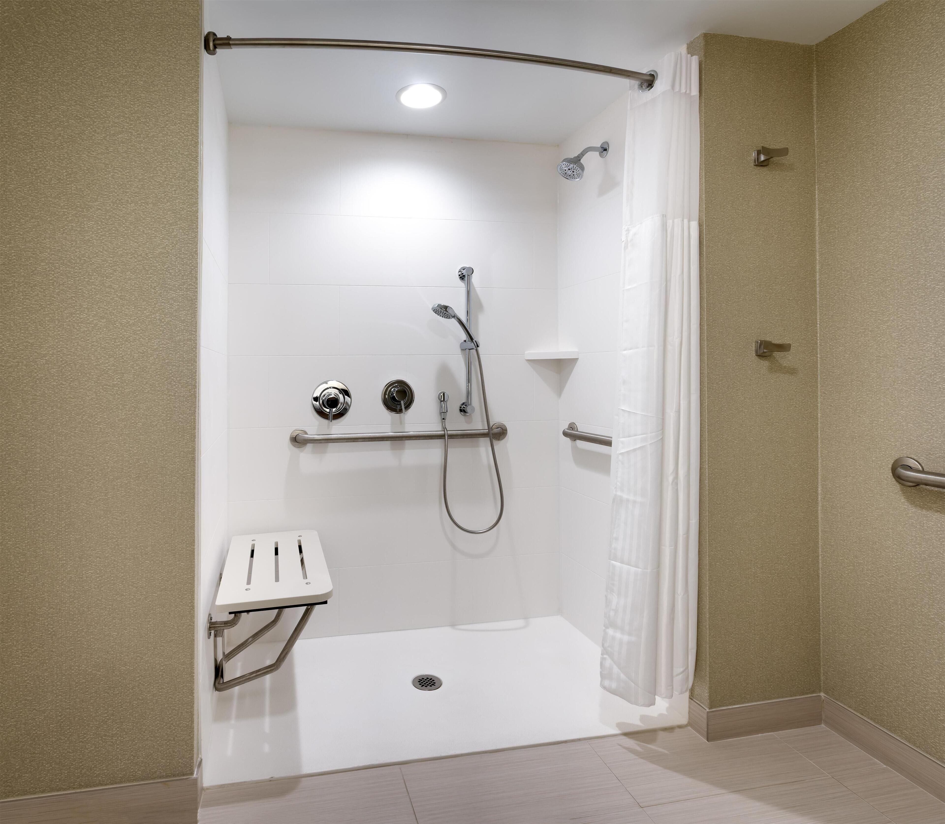 Une douche à l’italienne équipée d’une barre d’appui, d’un pommeau de douche amovible et d’un siège fixé au mur.