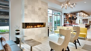 A modern living room with a fireplace, seating area, and a view of the kitchen. - Hilton Garden Inn Boise Downtown (Boise)