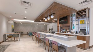 Uma área de bar moderna com um balcão comprido, vários bancos altos e uma tela de televisão.