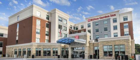 Un Hilton Garden Inn con diseño moderno, que presenta una combinación de fachadas de ladrillo y piedra, ventanas amplias y una entrada destacada con toldo azul.