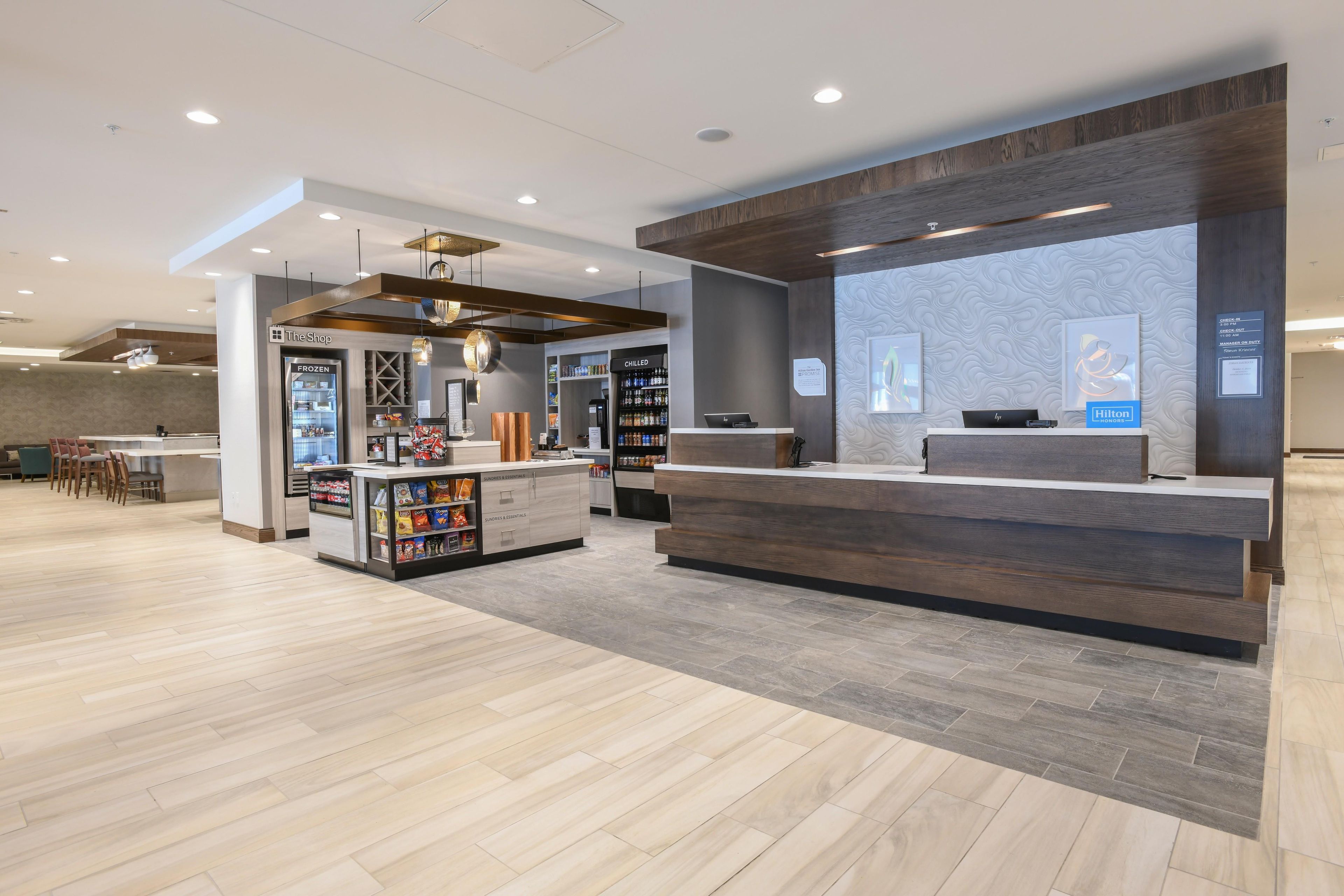 A hotel reception area with a modern design, including a reception desk, a minibar, and a seating area with tables and chairs.