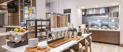 A modern breakfast bar with a variety of food items, a coffee station, and seating arrangements.