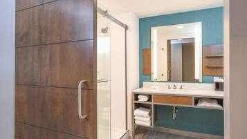 A modern bathroom with a wooden wardrobe, a glass shower enclosure, a white sink with a mirror, and a teal accent wall.