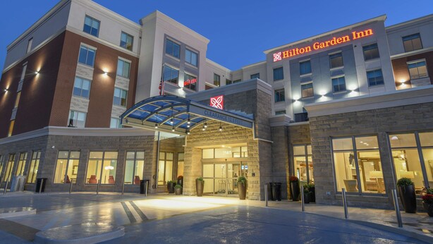 Entrada de um hotel com uma placa legível indicando "Hilton Garden Inn" e uma área de acesso coberta.