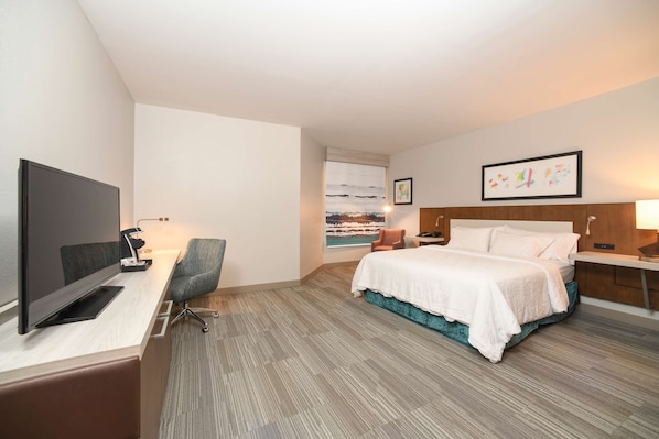 A hotel room with a bed, desk, chair, TV, and artwork on the walls.