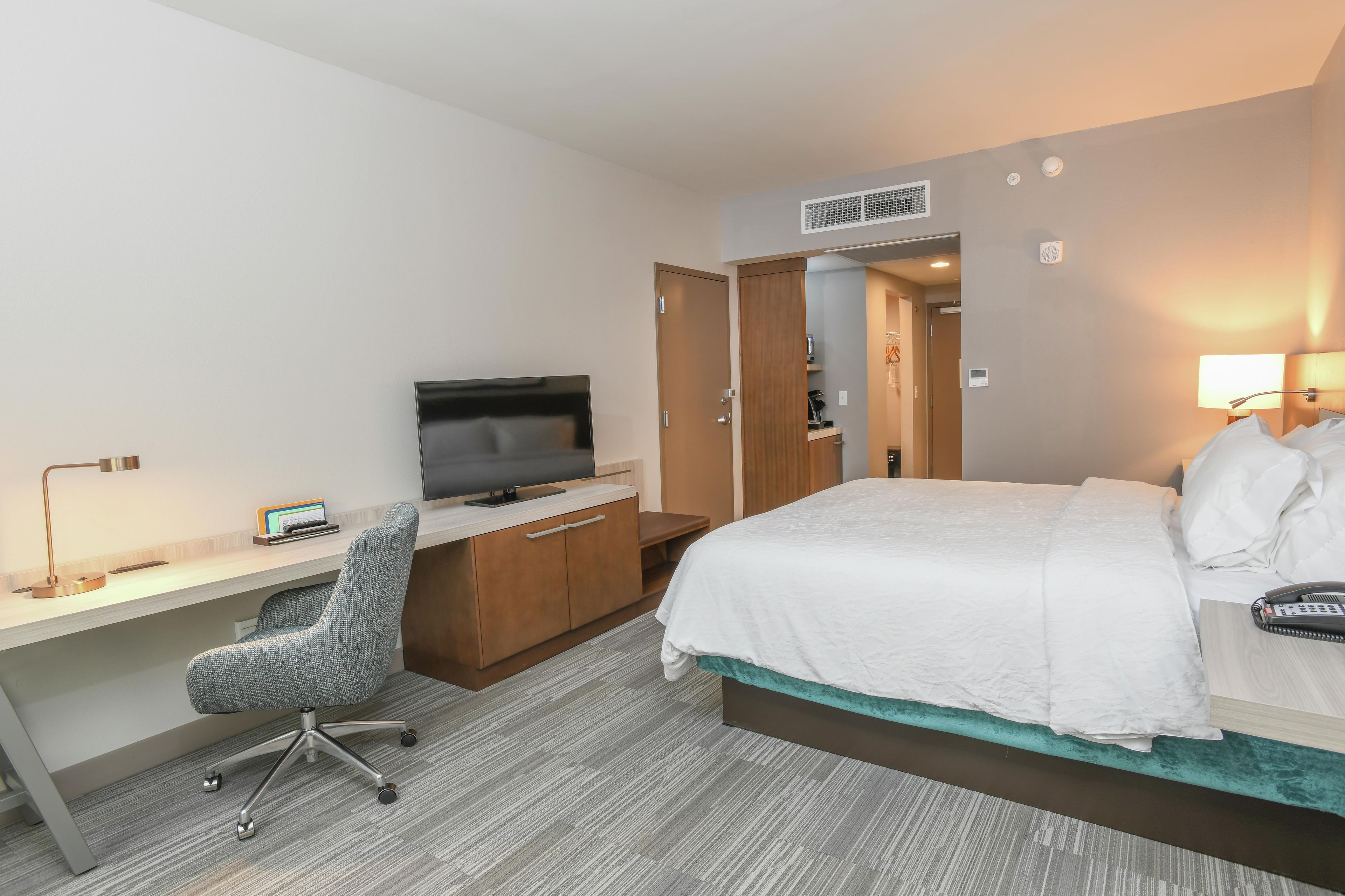 Ett hotellrum med en säng, ett skrivbord, en stol, en tv och en dörr till badrummet.