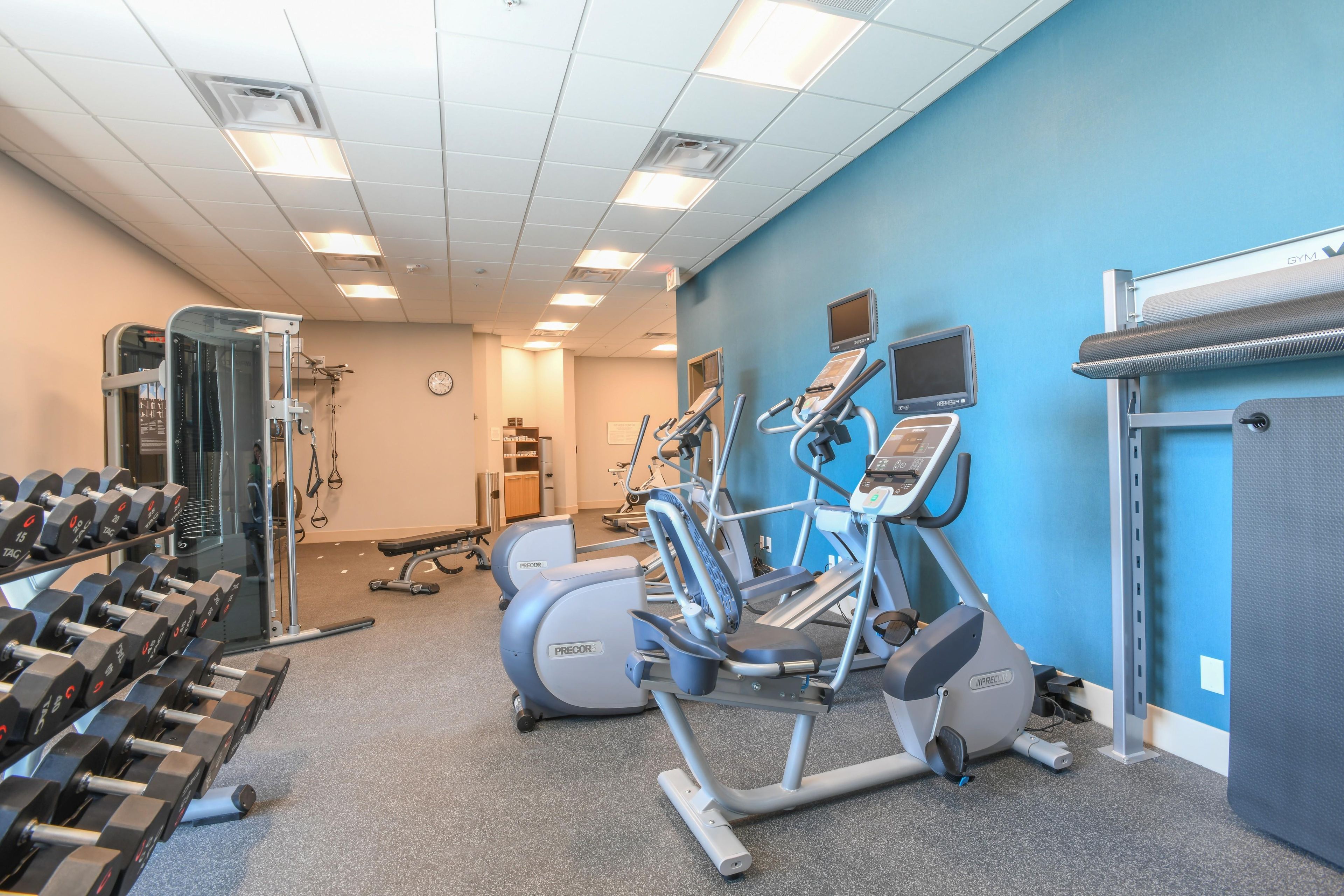 Une salle de sport équipée de tapis de course, de vélos elliptiques et de poids libres.